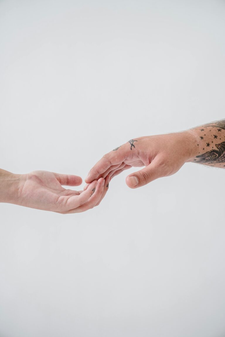 A touching close-up of tattooed and non-tattooed hands reaching towards each other.